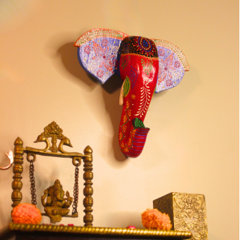 Red and blue hand-painted wooden elephant face wall hanging above Indian traditional setup