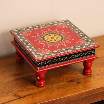 Wooden chowki hand painted in red with a mandala centrepiece and black-and-white geometric border, standing on four short carved legs.