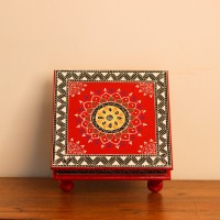 Wooden chowki hand painted in red with a mandala centrepiece and black-and-white geometric border, standing on four short carved legs.