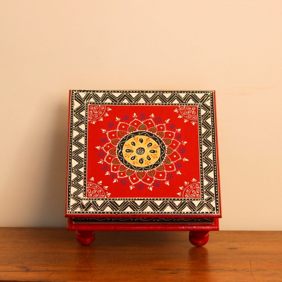 Wooden chowki hand painted in red with a mandala centrepiece and black-and-white geometric border, standing on four short carved legs.