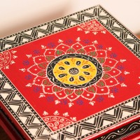 Wooden chowki hand painted in red with a mandala centrepiece and black-and-white geometric border, standing on four short carved legs.