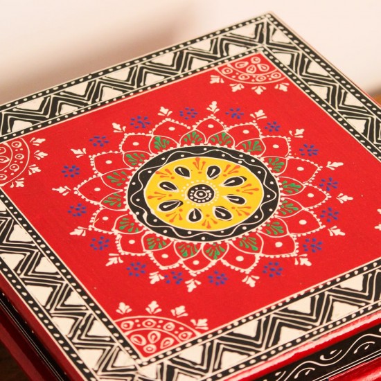 Wooden chowki hand painted in red with a mandala centrepiece and black-and-white geometric border, standing on four short carved legs.