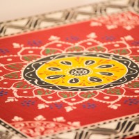 Wooden chowki hand painted in red with a mandala centrepiece and black-and-white geometric border, standing on four short carved legs.