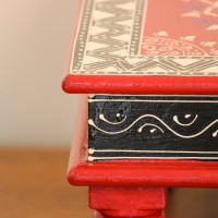 Wooden chowki hand painted in red with a mandala centrepiece and black-and-white geometric border, standing on four short carved legs.