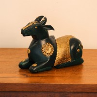Deep green wooden Nandi figurine with embossed brass work placed on a wooden table as a pooja or console accent
