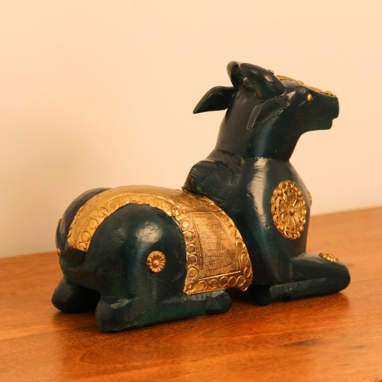 Deep green wooden Nandi figurine with embossed brass work placed on a wooden table as a pooja or console accent