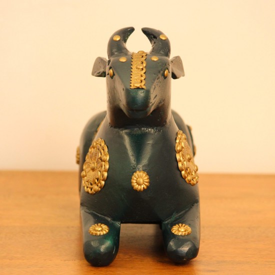 Deep green wooden Nandi figurine with embossed brass work placed on a wooden table as a pooja or console accent