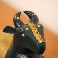 Deep green wooden Nandi figurine with embossed brass work placed on a wooden table as a pooja or console accent