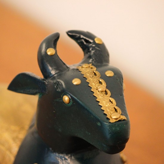 Deep green wooden Nandi figurine with embossed brass work placed on a wooden table as a pooja or console accent