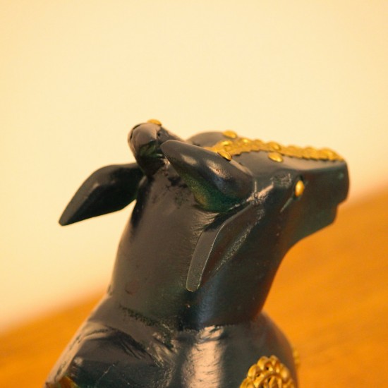 Deep green wooden Nandi figurine with embossed brass work placed on a wooden table as a pooja or console accent