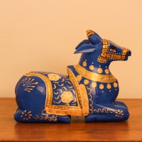 Blue Nandi Figurine with Golden Finish Styled on Table Cobalt blue wooden Nandi figurine with gold painted detailing placed on a wooden table as a pooja or console accent.