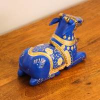 Blue Nandi Figurine with Golden Finish Styled on Table Cobalt blue wooden Nandi figurine with gold painted detailing placed on a wooden table as a pooja or console accent.