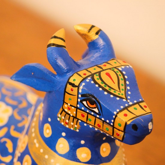 Blue Nandi Figurine with Golden Finish Styled on Table Cobalt blue wooden Nandi figurine with gold painted detailing placed on a wooden table as a pooja or console accent.