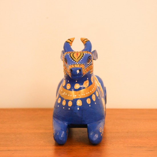 Blue Nandi Figurine with Golden Finish Styled on Table Cobalt blue wooden Nandi figurine with gold painted detailing placed on a wooden table as a pooja or console accent.