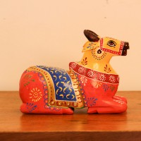Multicolour Nandi Figurine Styled on Table Hand-painted multicolour wooden Nandi figurine with an orange-red body placed on a wooden table as a pooja or console accent.