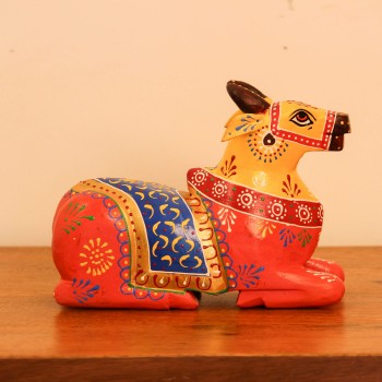 Multicolour Nandi Figurine Styled on Table Hand-painted multicolour wooden Nandi figurine with an orange-red body placed on a wooden table as a pooja or console accent.