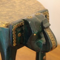 Elephant Stool – Green with Embossed Brass, Side View Side view of the elephant stool, showing the raised trunk, the brass-embossed seat and the brass side panel set between the dark green legs.