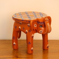 Hand Painted Burnt Orange Elephant Stool Styled on Table Hand-painted burnt orange-brown wooden elephant stool placed on a wooden table as a side stool or display stand.