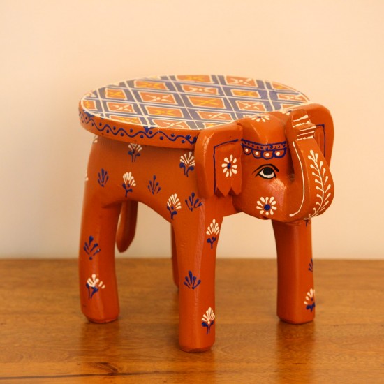 Hand Painted Burnt Orange Elephant Stool Styled on Table Hand-painted burnt orange-brown wooden elephant stool placed on a wooden table as a side stool or display stand.