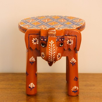 Hand-painted burnt orange-brown wooden elephant stool placed on a wooden table as a side stool or display stand.