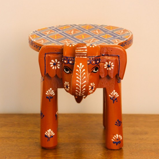 Hand Painted Burnt Orange Elephant Stool Styled on Table Hand-painted burnt orange-brown wooden elephant stool placed on a wooden table as a side stool or display stand.