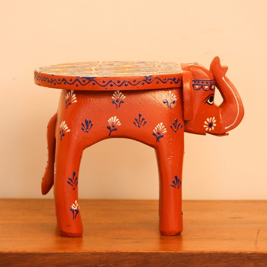 Hand Painted Burnt Orange Elephant Stool Styled on Table Hand-painted burnt orange-brown wooden elephant stool placed on a wooden table as a side stool or display stand.