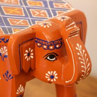 Hand Painted Burnt Orange Elephant Stool Styled on Table Hand-painted burnt orange-brown wooden elephant stool placed on a wooden table as a side stool or display stand.