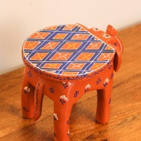 Hand Painted Burnt Orange Elephant Stool Styled on Table Hand-painted burnt orange-brown wooden elephant stool placed on a wooden table as a side stool or display stand.