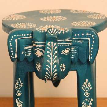 Teal blue hand-painted wooden elephant stool placed on a wooden table as a side stool or display stand.