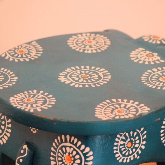 Teal blue hand-painted wooden elephant stool placed on a wooden table as a side stool or display stand.